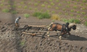Ein Foto aus der Miniaturausstellung, auf dem ein Mann mit seinem Pferd einen Esch bearbeitet